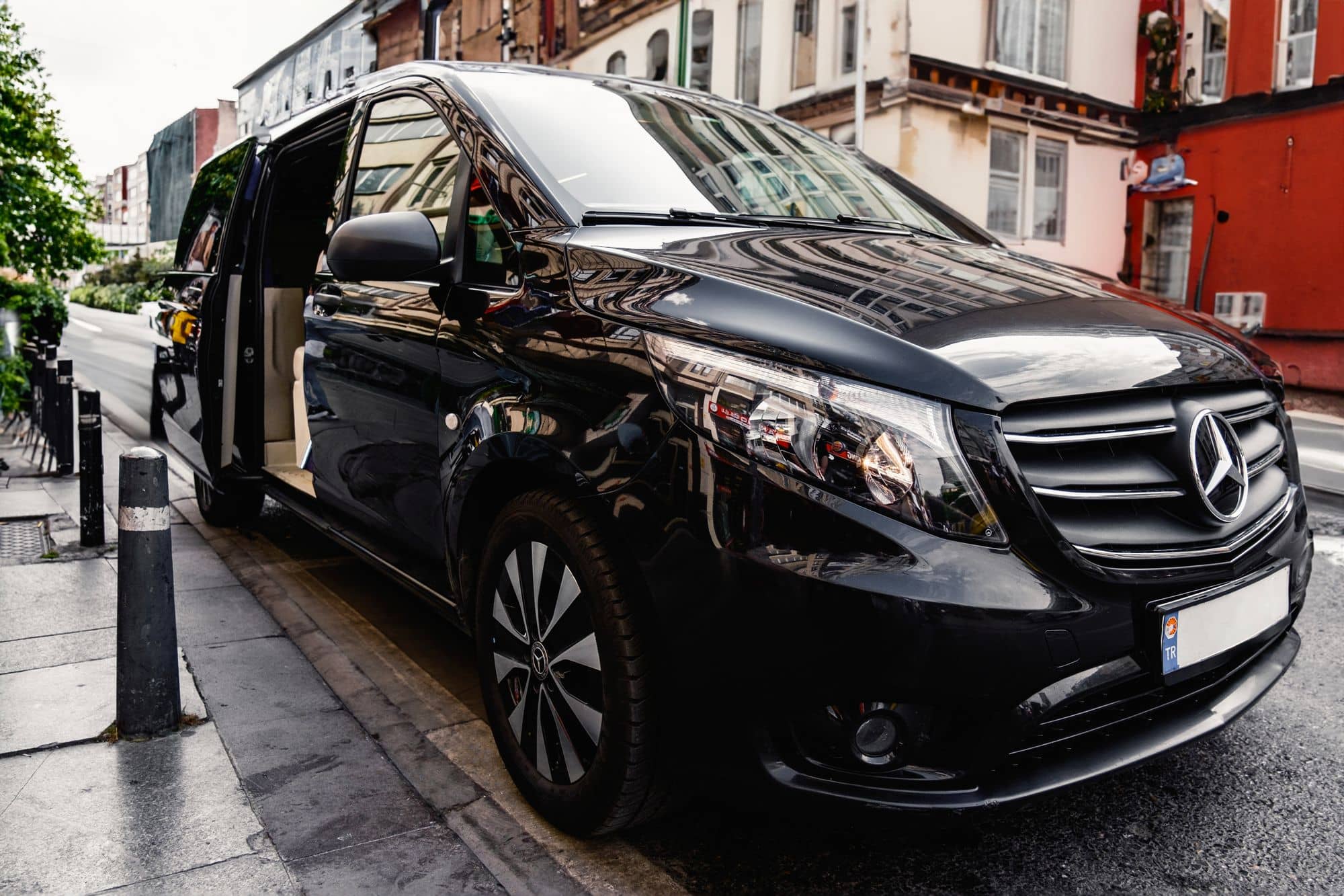 A glossy black Mercedes-Benz chauffeur van parked door-open on a European street