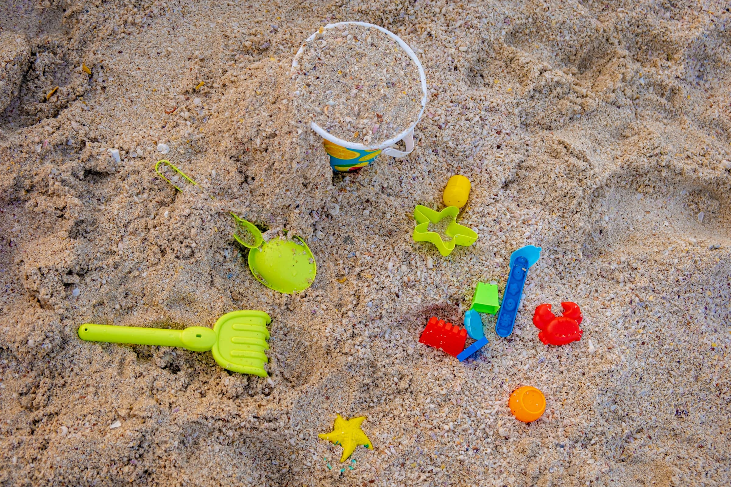 Sand toys half-buried in coarse, shell-flecked sand