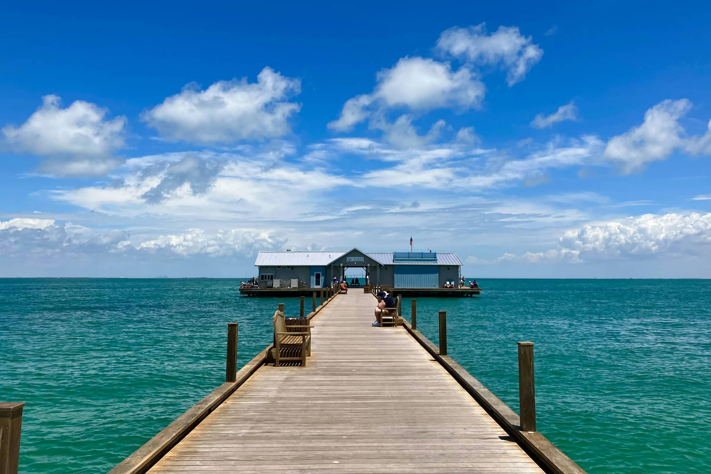 Wooden pier running out to a small blue pavilion over clear green gulf water