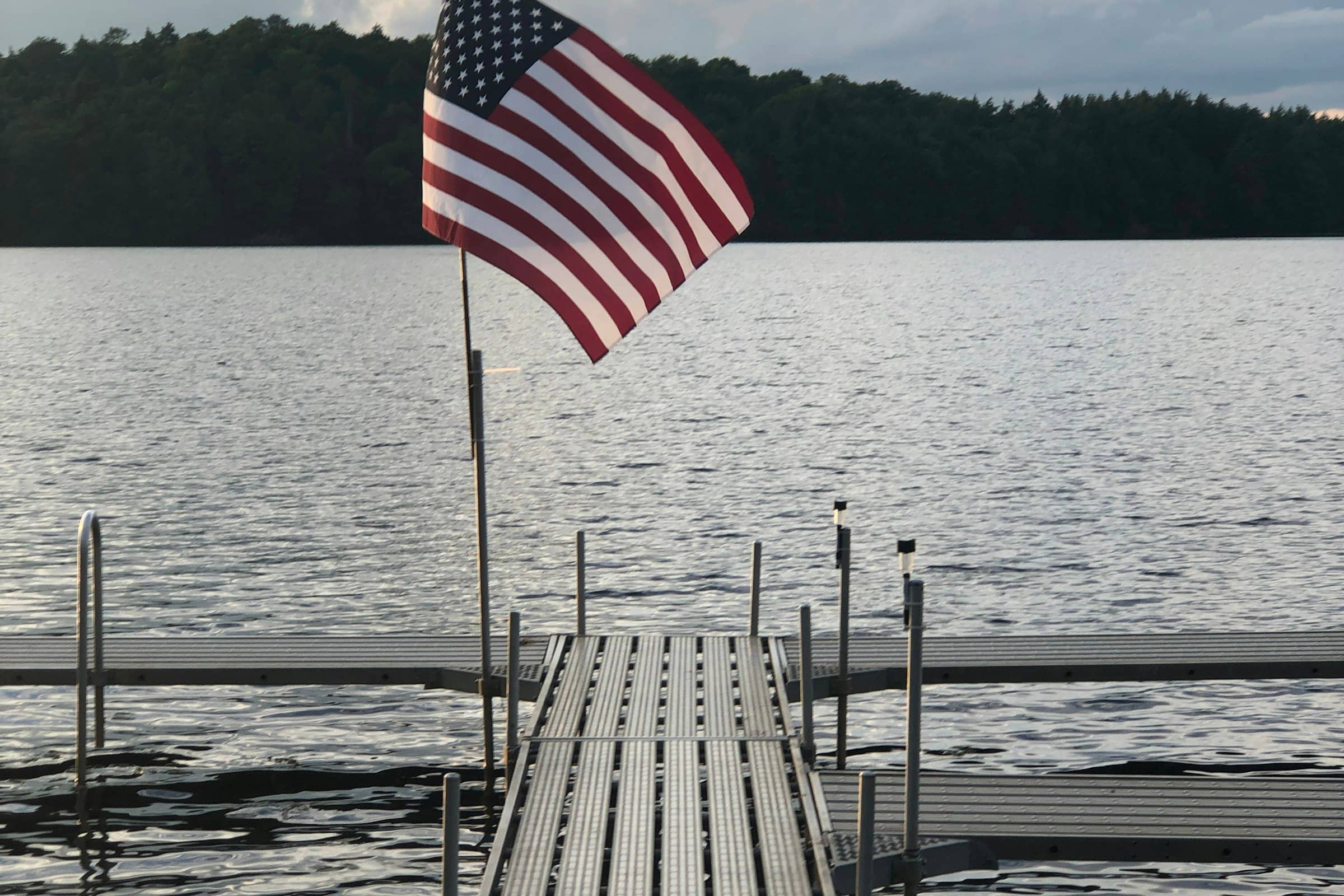 An American flag flying over a quiet dock on still water