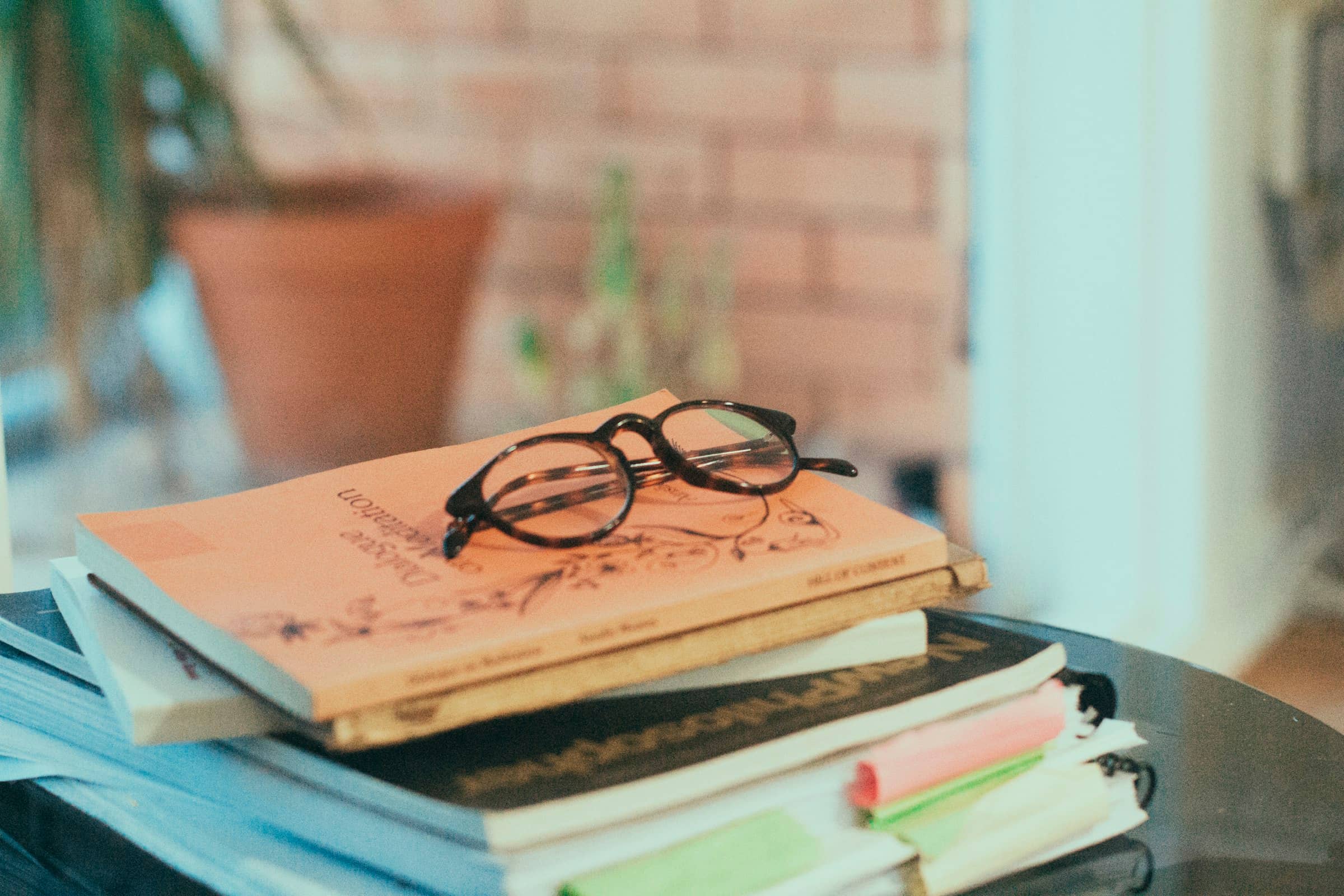 Reading glasses resting on a stack of well-used books by a bright window
