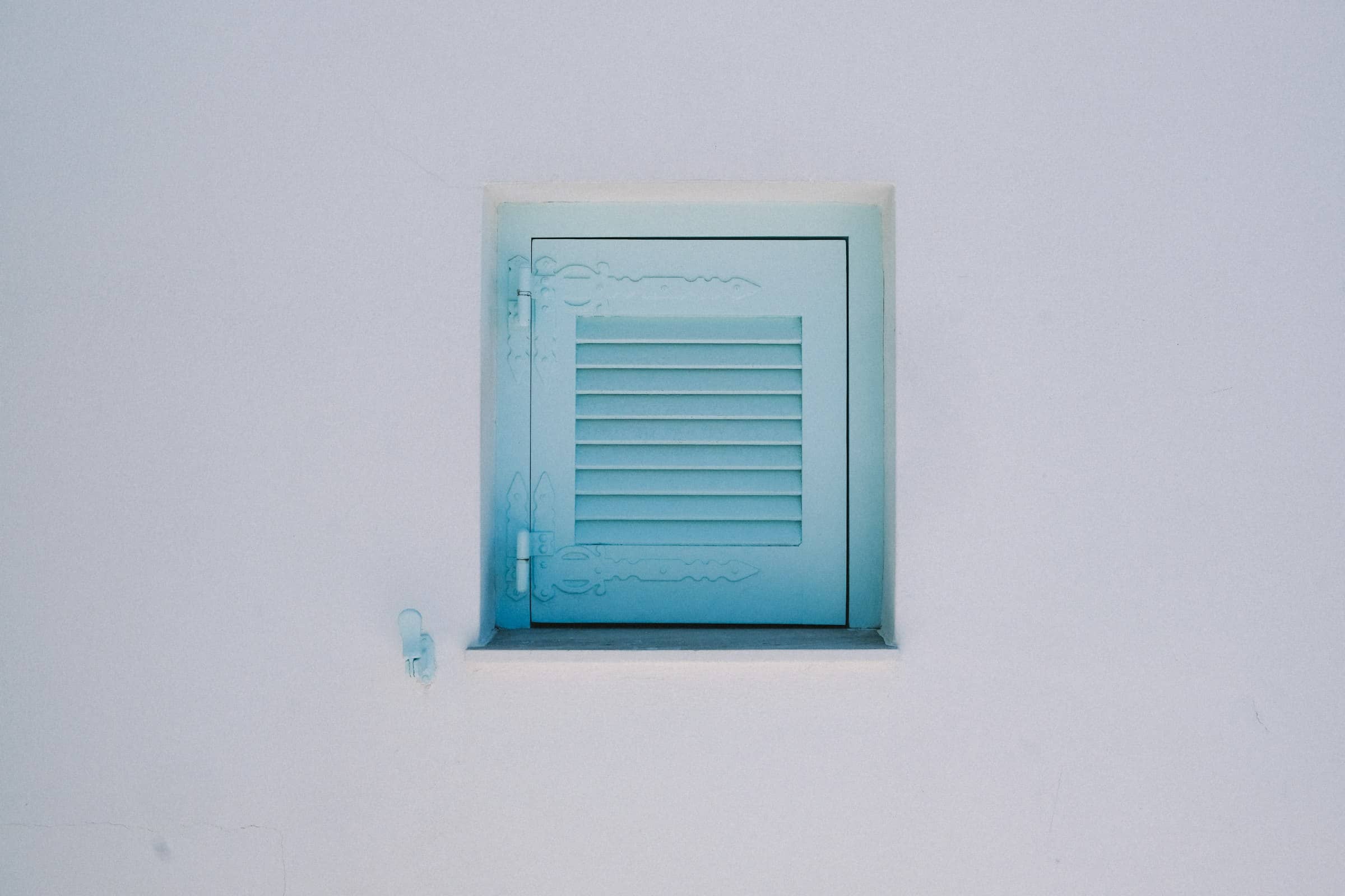 A small pale-blue louvered shutter set in a plain white wall