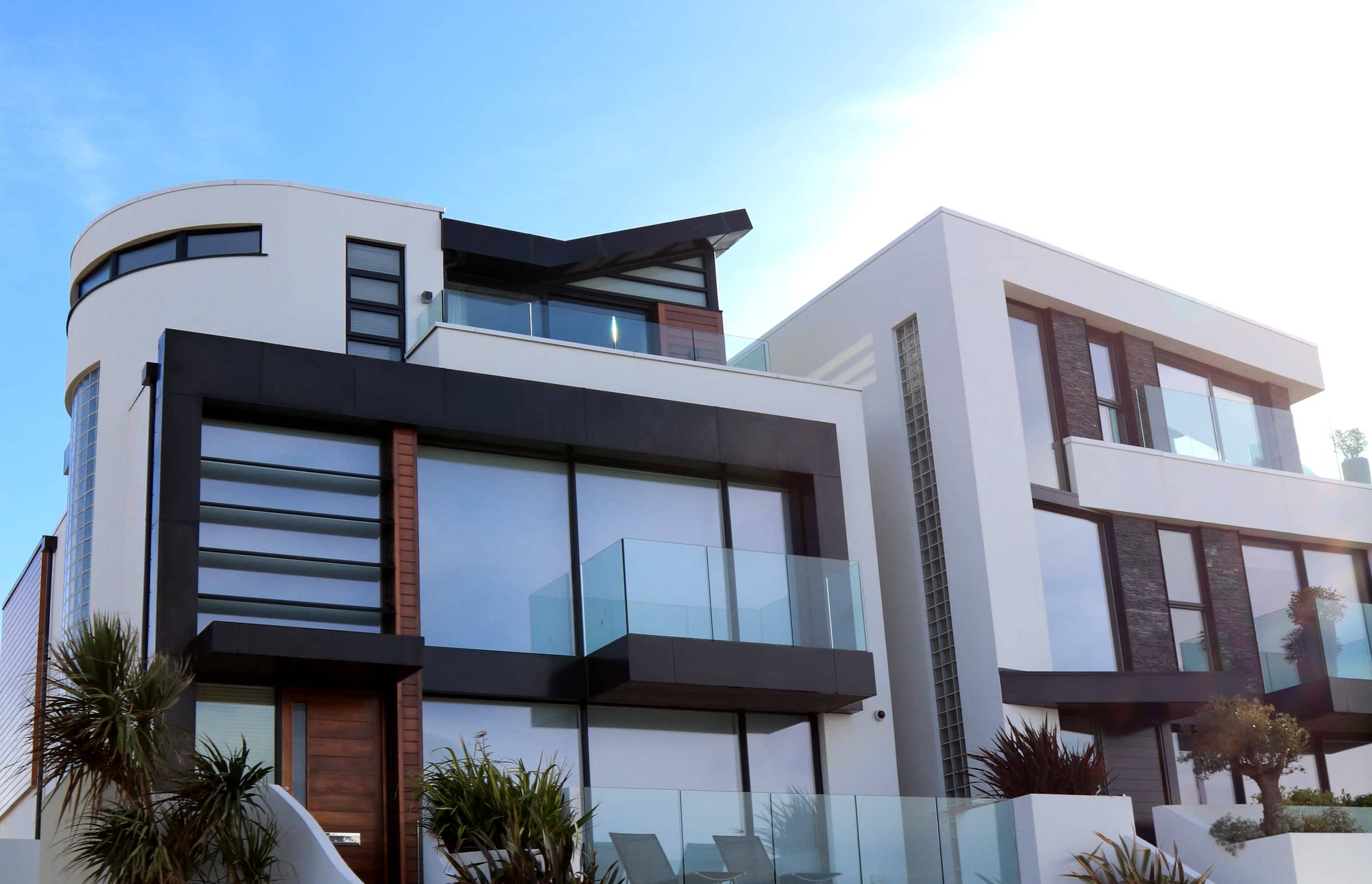 Two contemporary residences in full sun, white render and timber behind glass balustrades