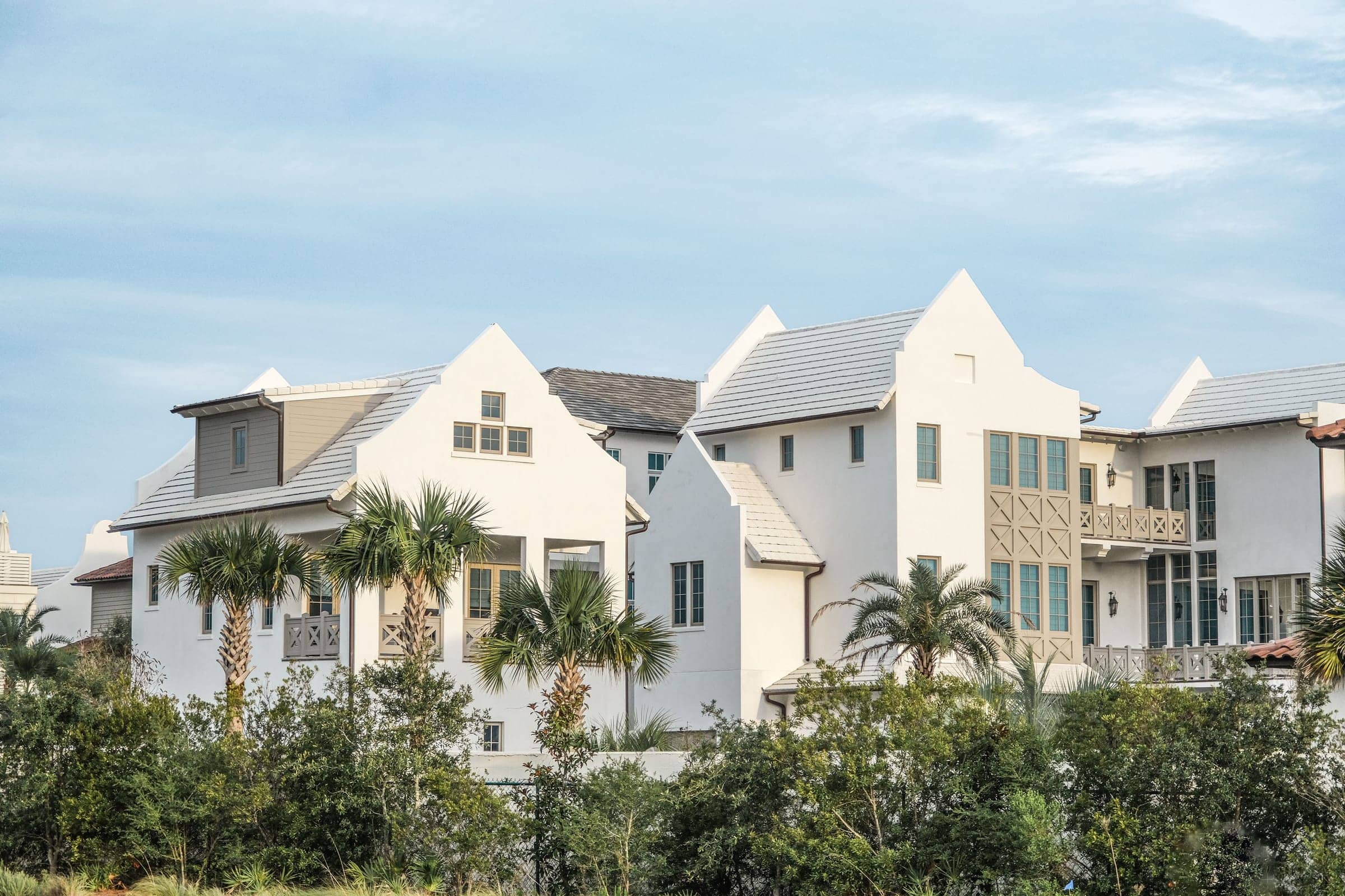 White stucco gables and parapet rooflines at Alys Beach in warm light, sabal palms rising against the facades