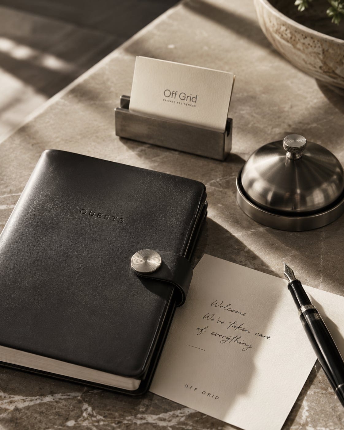An OFF GRID guest notebook, concierge bell and a handwritten welcome note on a sunlit marble console