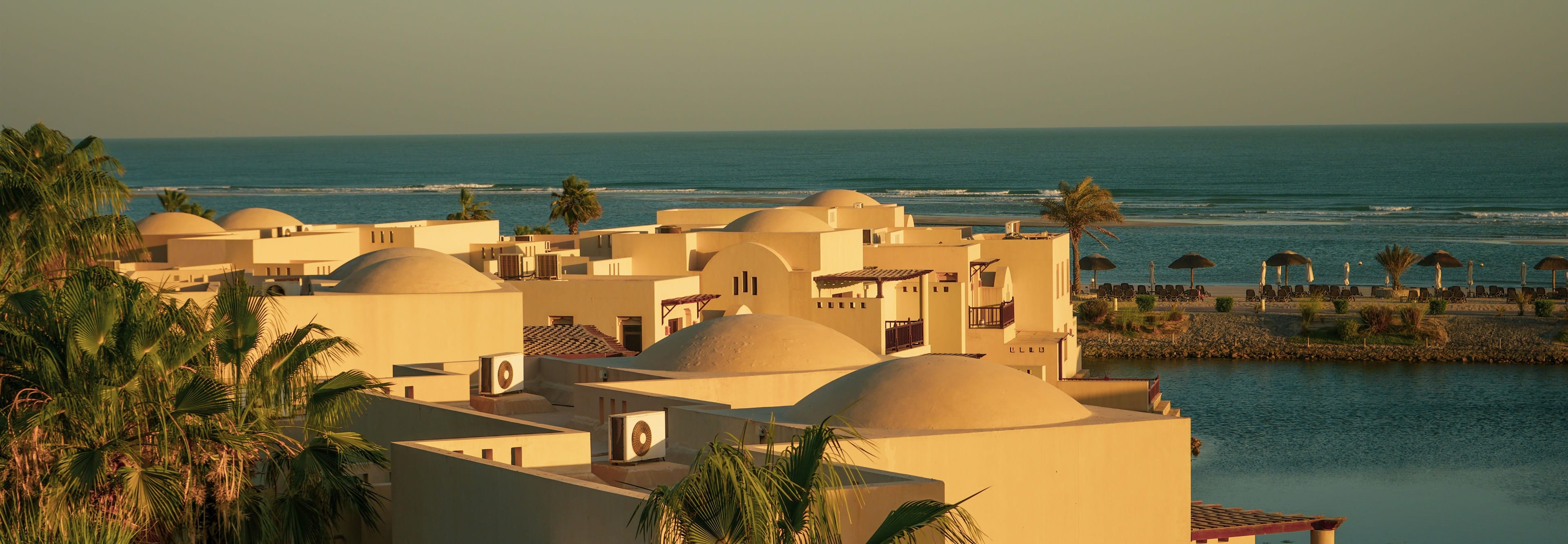 Domed villas stepping down to the sea at golden hour, palms in the foreground