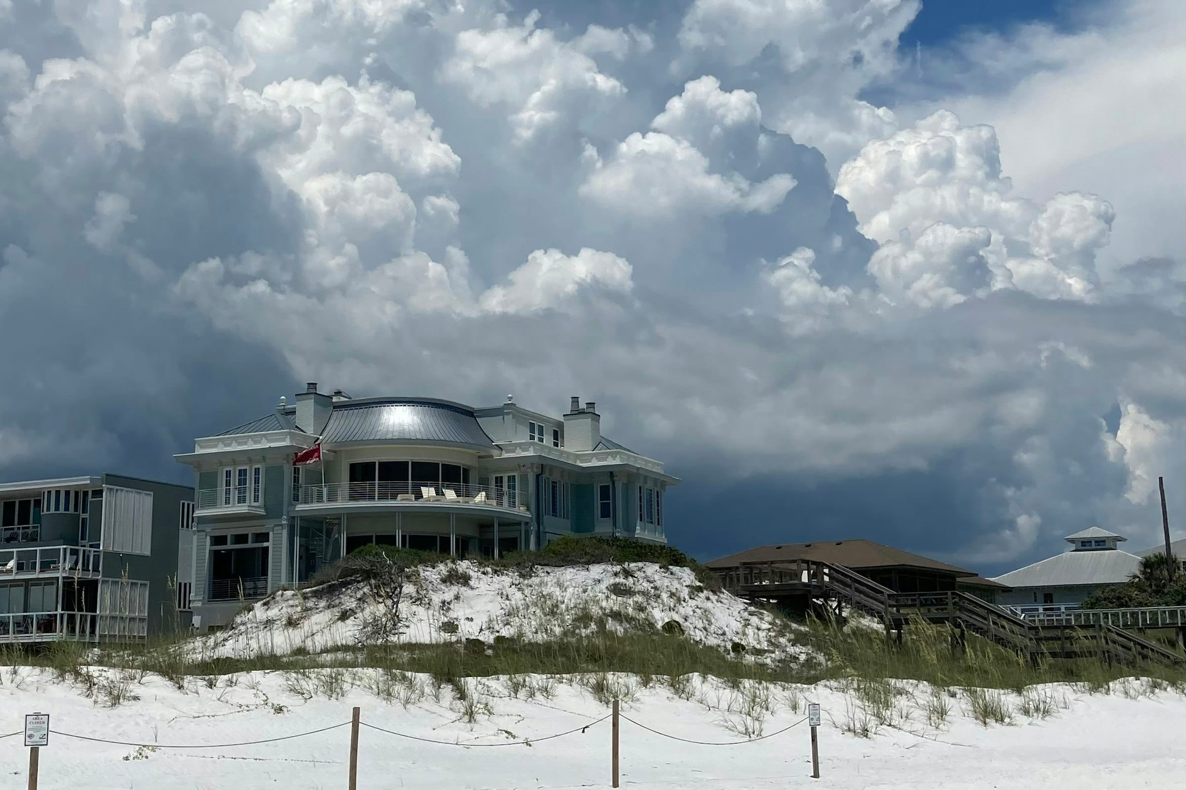 Pale beach houses on a white dune under a building summer storm