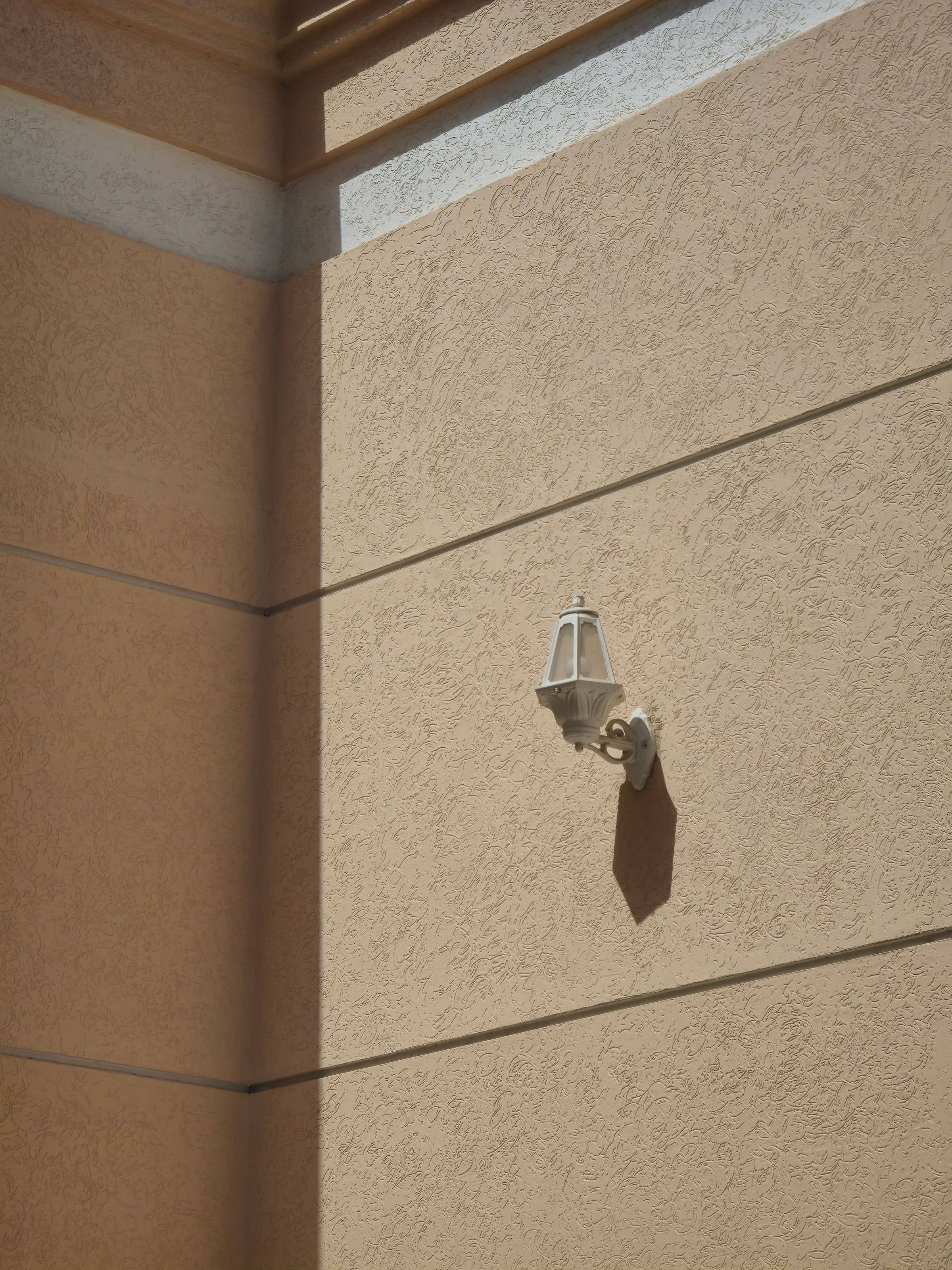 A lantern casting a long shadow across a warm stucco wall in low sun