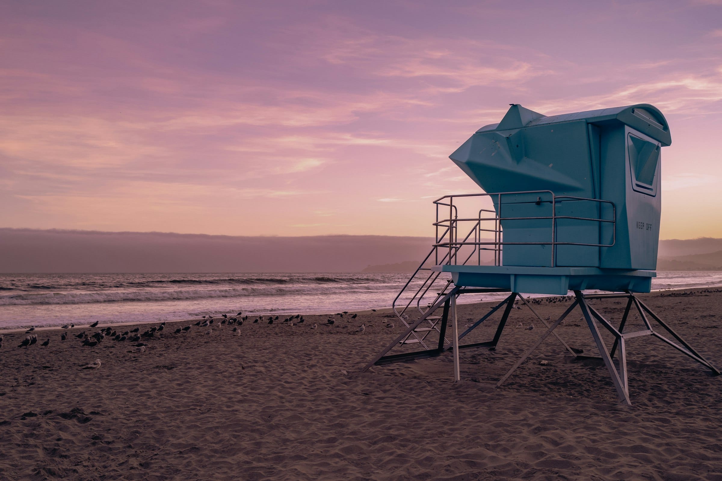 An empty blue lifeguard tower on a bare beach at dusk