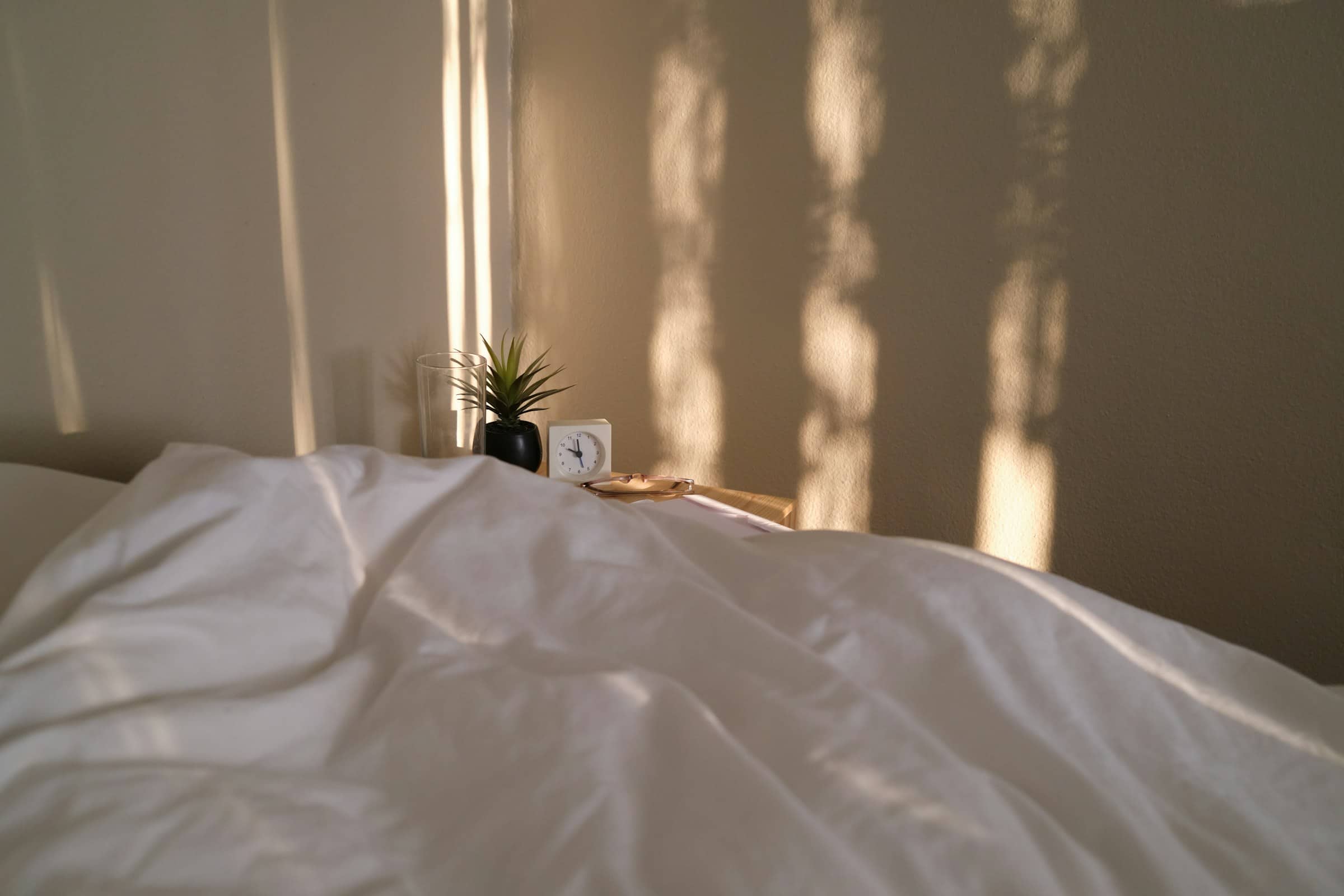 White bedding in raking evening light, a small clock on the bedside shelf